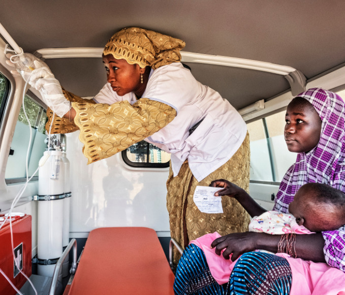 Nurse preparing an ambulance while women and child sit inside waiting.