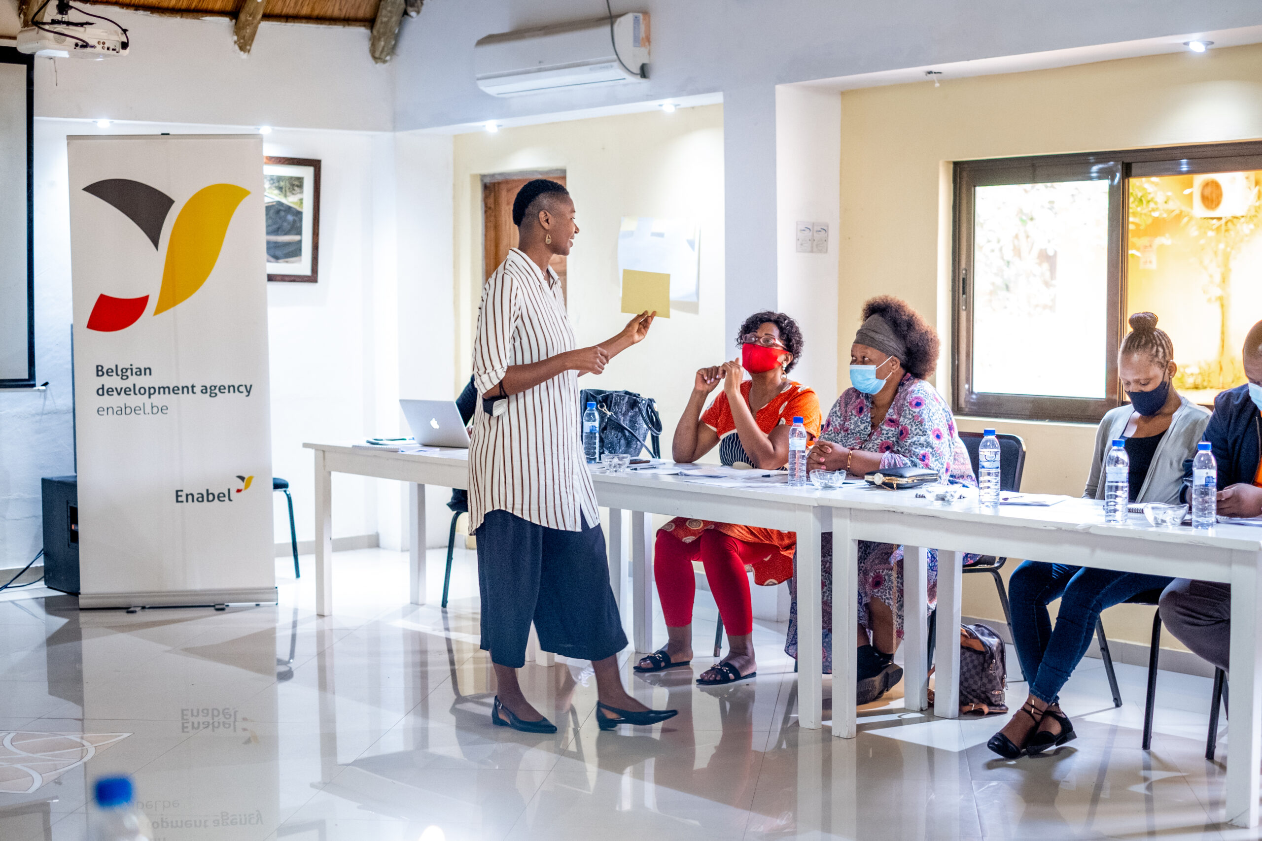Colleagues and partners in Mozambique sitting at a table. One women is standing up and speaking.
