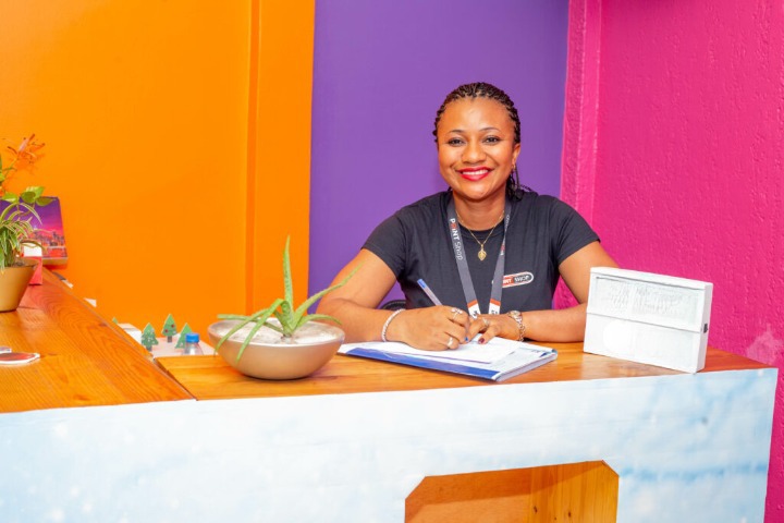 Woman sitting behind a desk, smiling at someone approaching her.