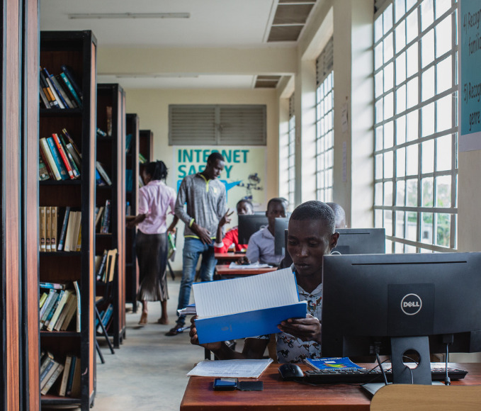 Boy sits behind a computer at a public library in Uganda.