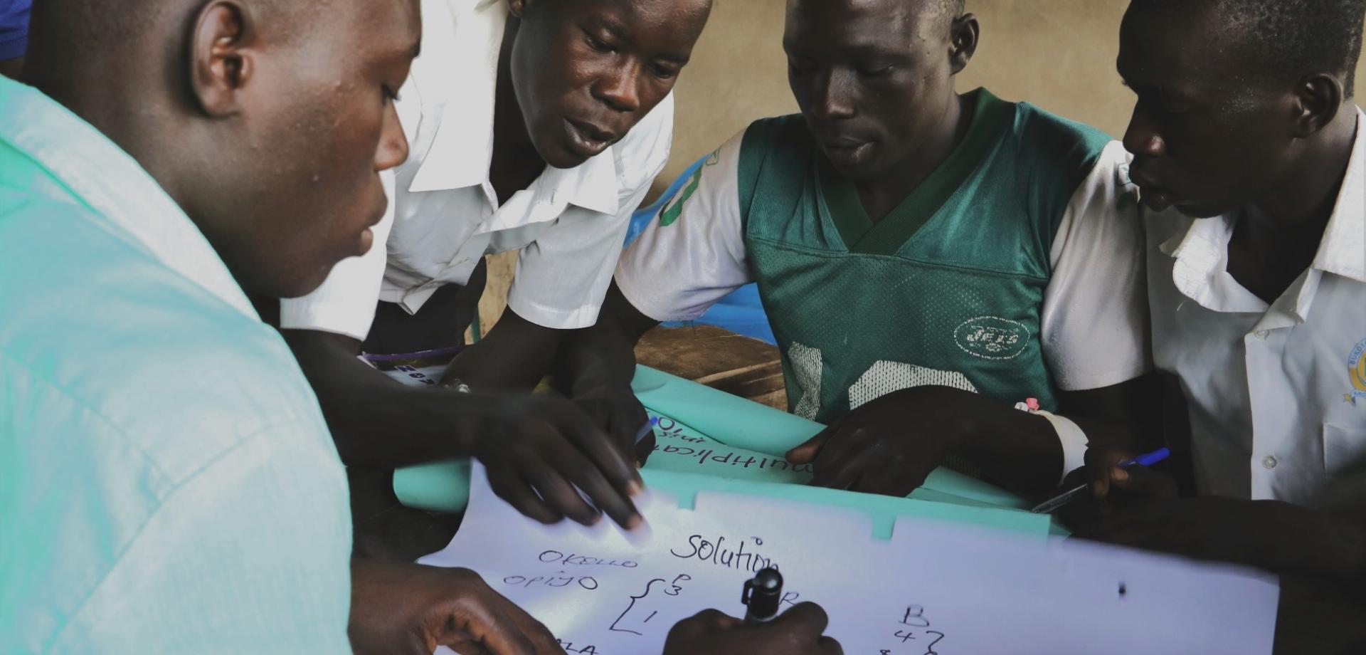 students in Uganda sitting around a table working as a group to solve a problem.
