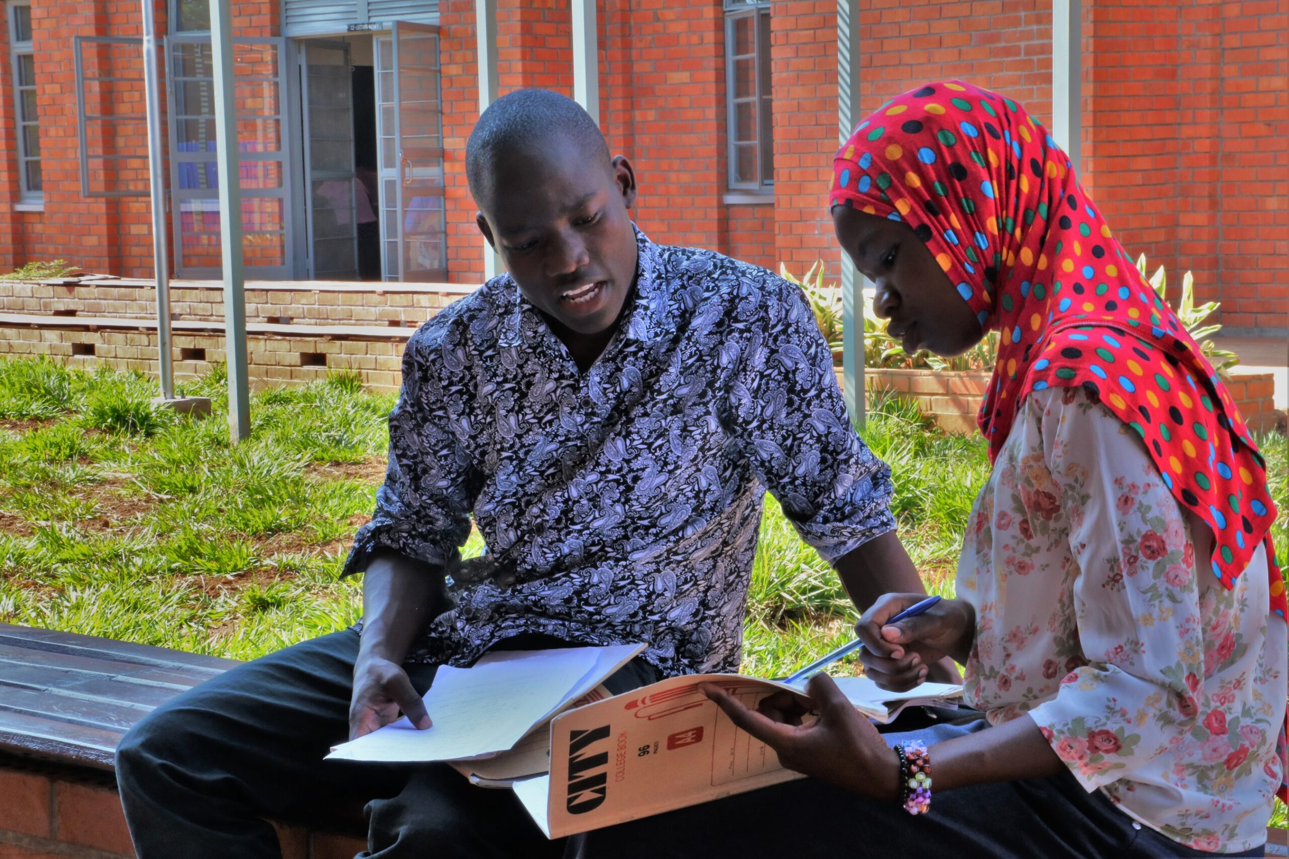 boy and a girl are working together in the open green space of Kaliro National Teachers College in Uganda.