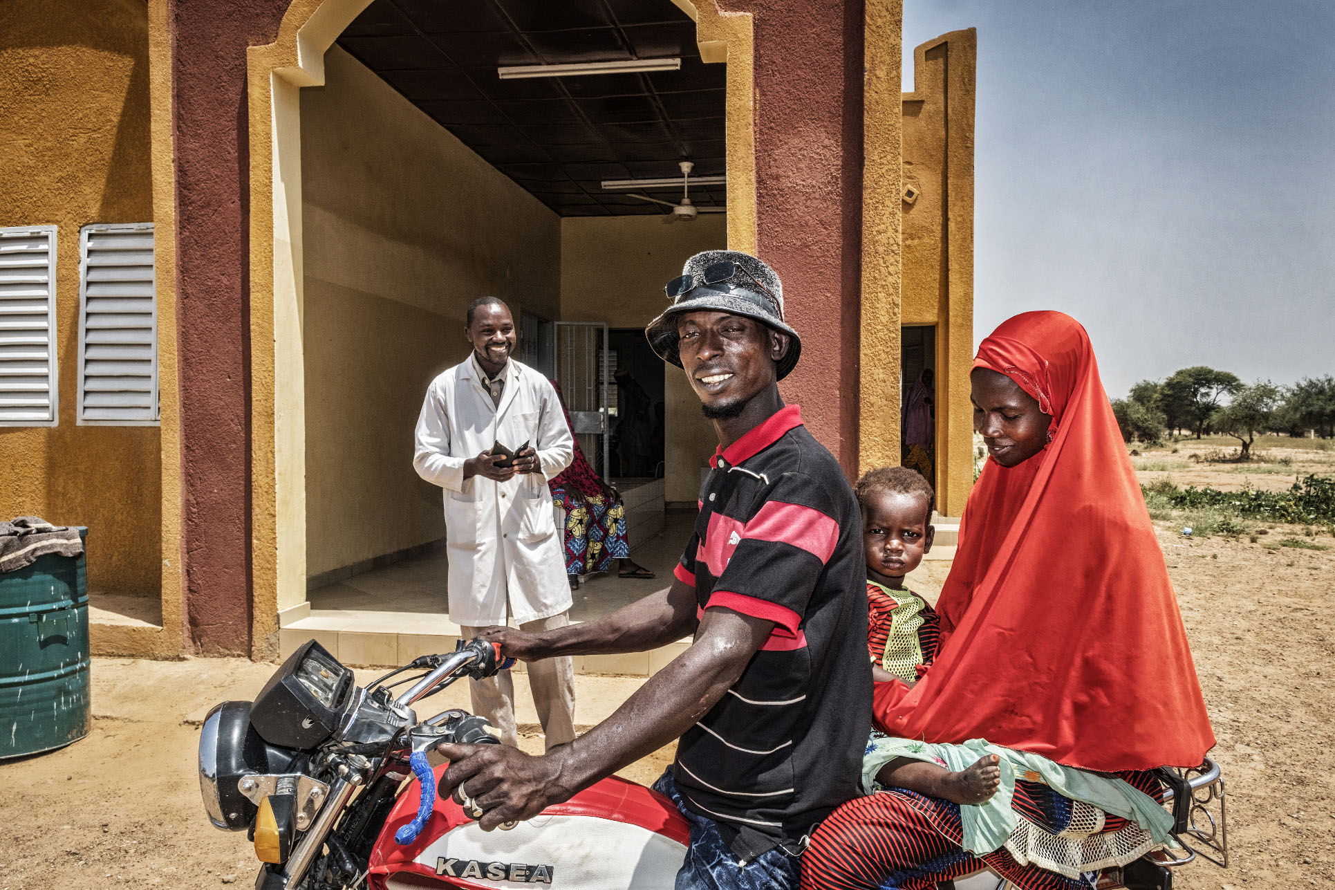 Doctor standing outside of a medical centre in Niger while a family arrives on a motortaxi